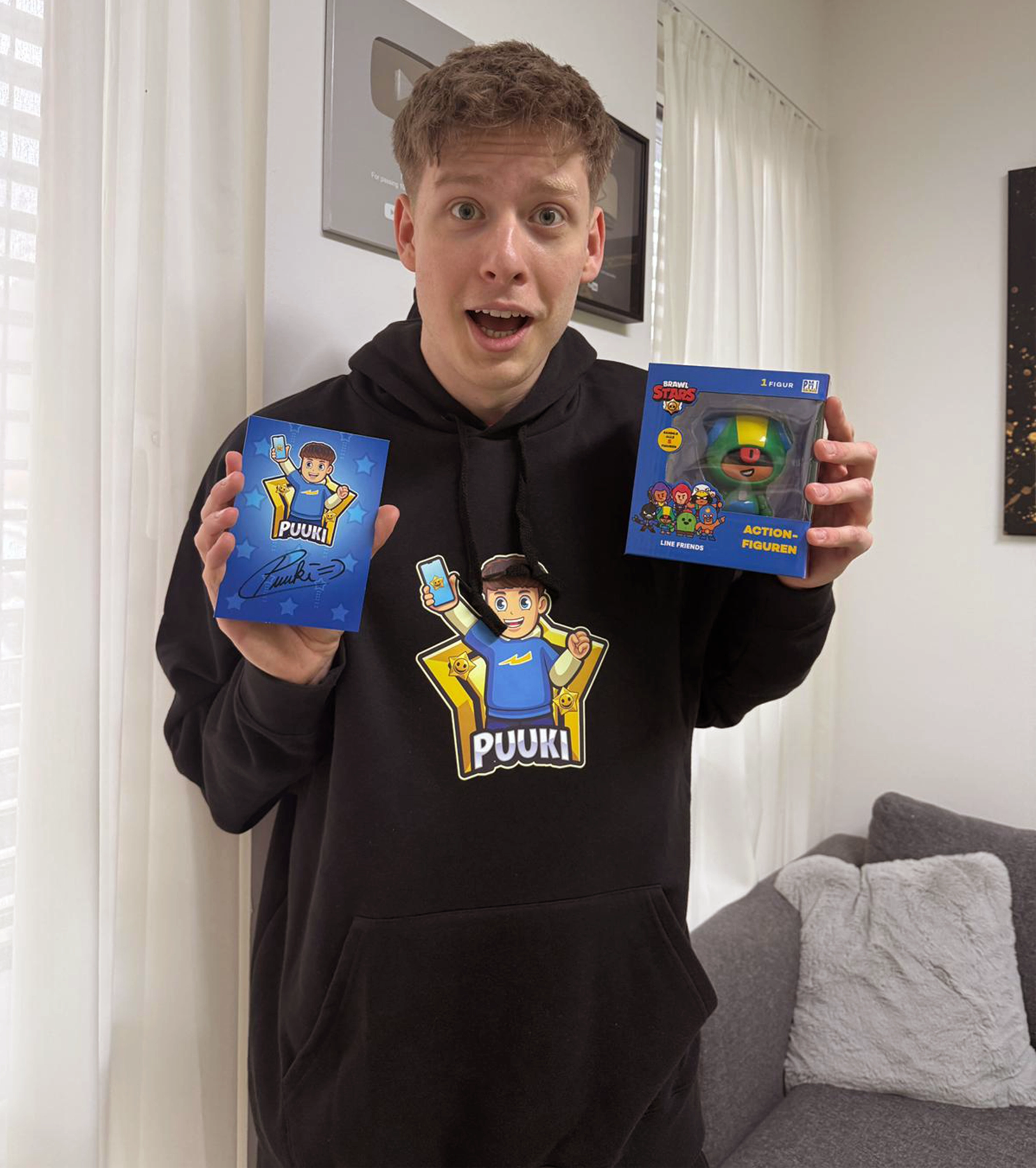 Creator Puuki praesentiert seinen schwarzen Hoodie mit Comic-Motiv, eine signierte Autogrammkarte und eine Brawl Stars Action-Figur – ideales Fanpaket für junge Gaming-Fans.