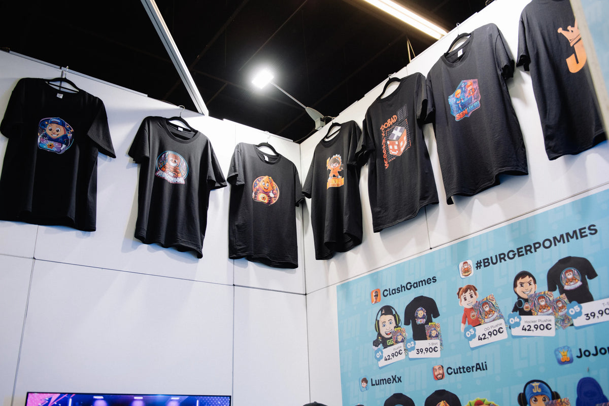 Schwarze Creator T-Shirts hängen über der Produktübersicht am LunyMerch Messestand auf der gamescom 2026